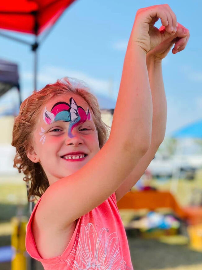 young girl posing like a horse, her face is painted like a unicorn