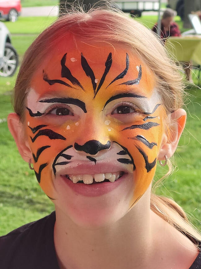 young girl smiling at camera, her face is painted like a tiger